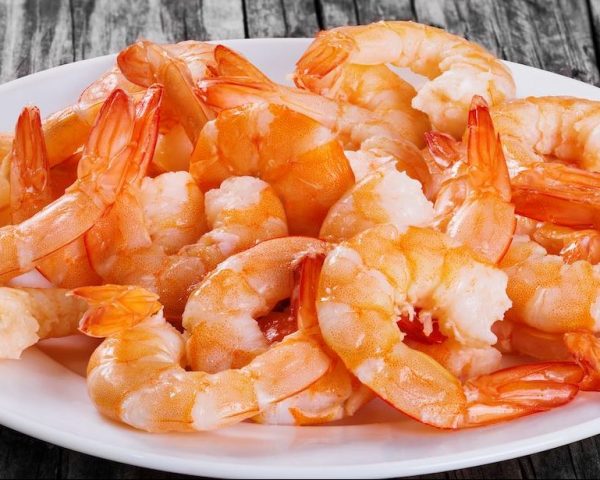 boiled tails of king shrimps on a white platter on an old rustic table, close-up, studio lights